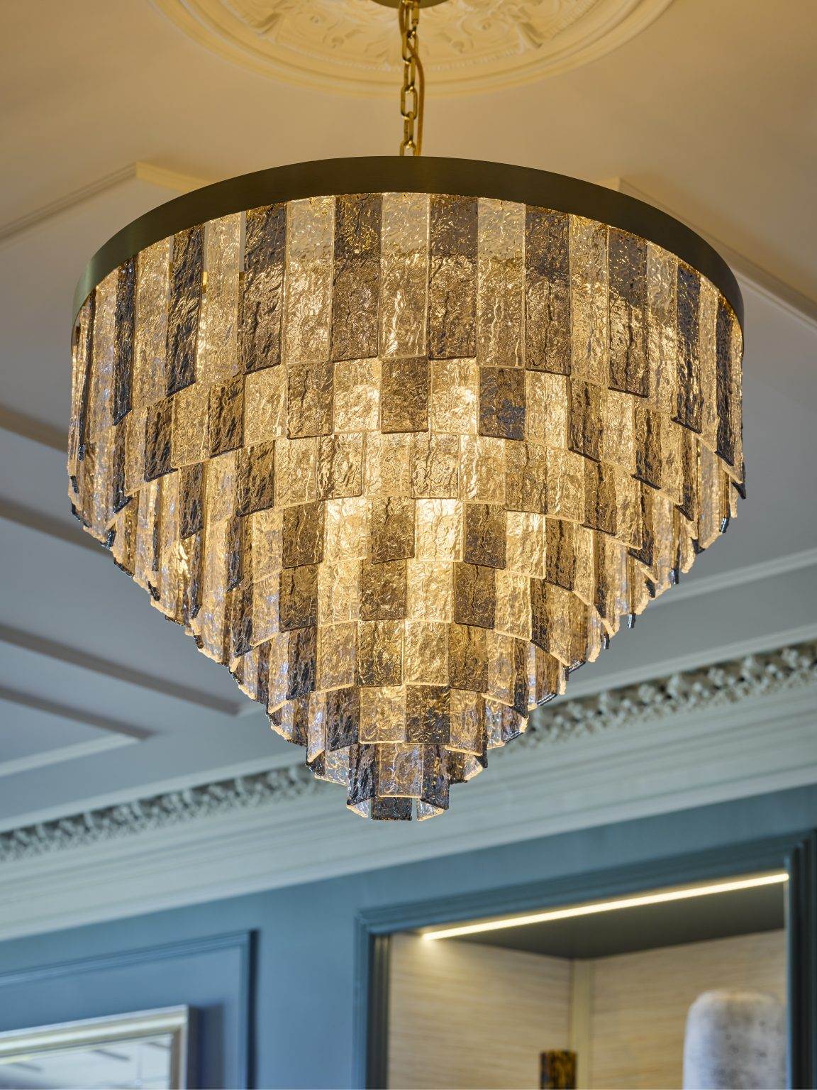 Luxury chandelier used in hospitality fit-out, featuring textured glass panels and brass accents for a sophisticated lighting solution.