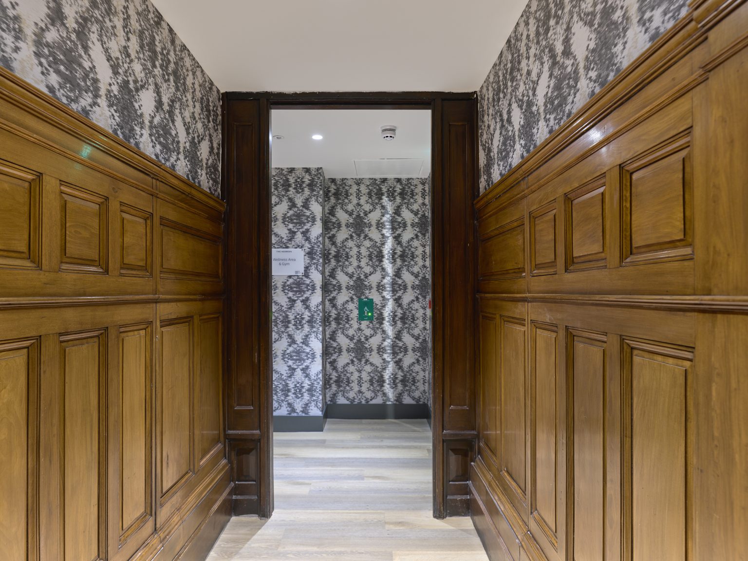 Hallway with rich wooden panelling and patterned wallpaper, creating a classic ambience in this hospitality interior.