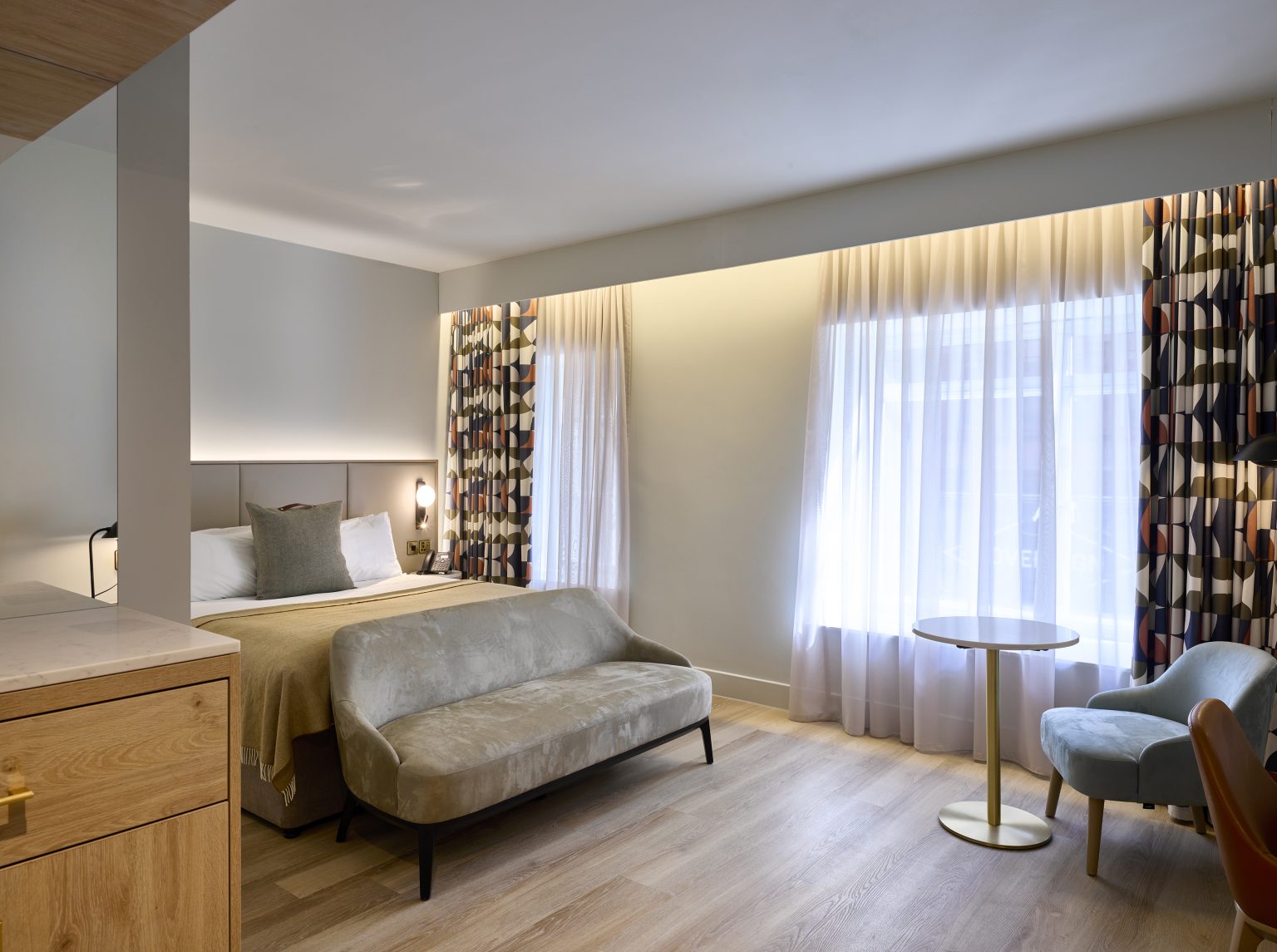 Spacious hotel room with luxurious bed and geometric curtains, reflecting modern hospitality interior design trends.