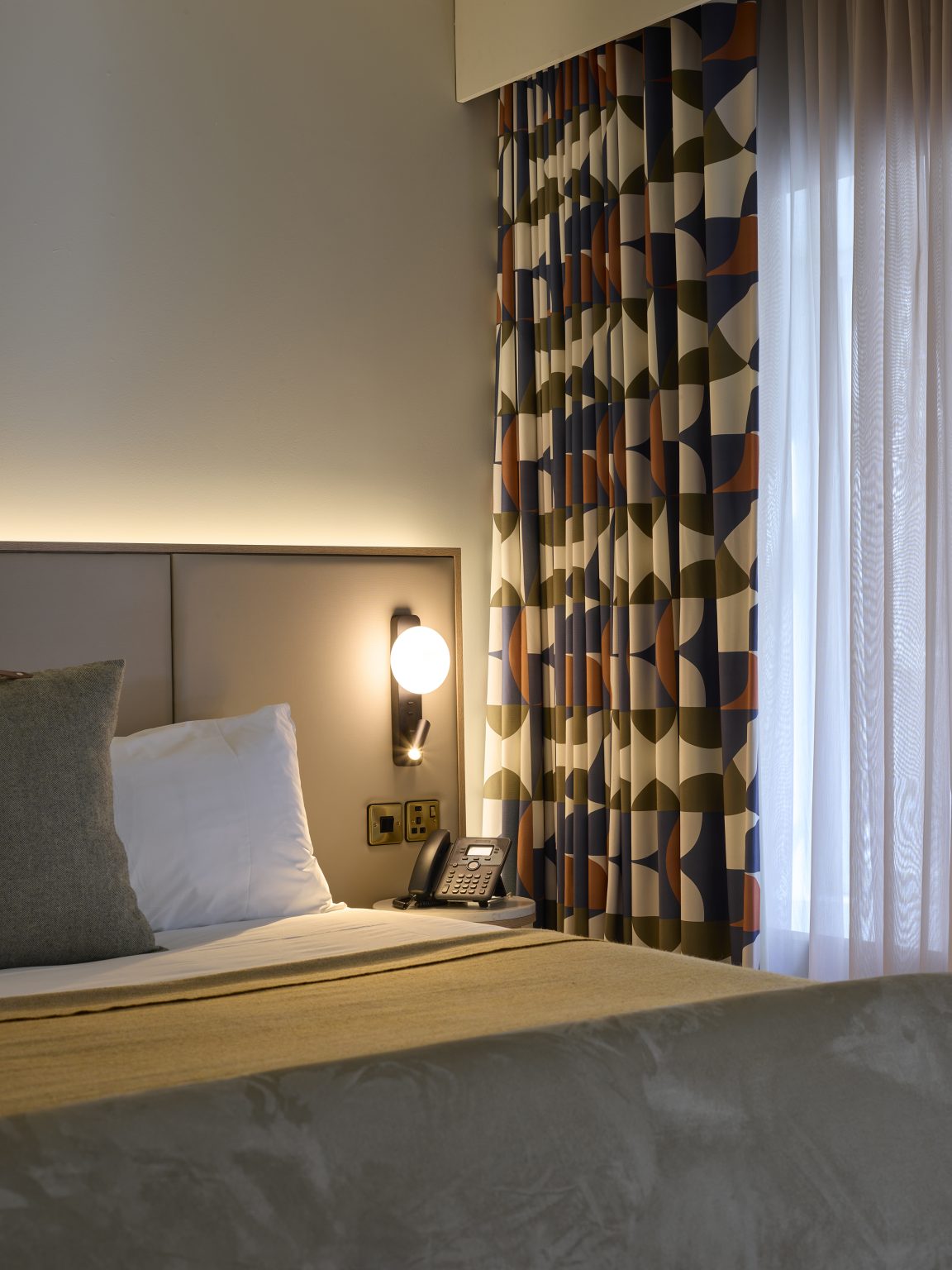 Stylish king-sized bed with bedside lamps and patterned curtains, illustrating the inviting comfort of the hospitality interior.