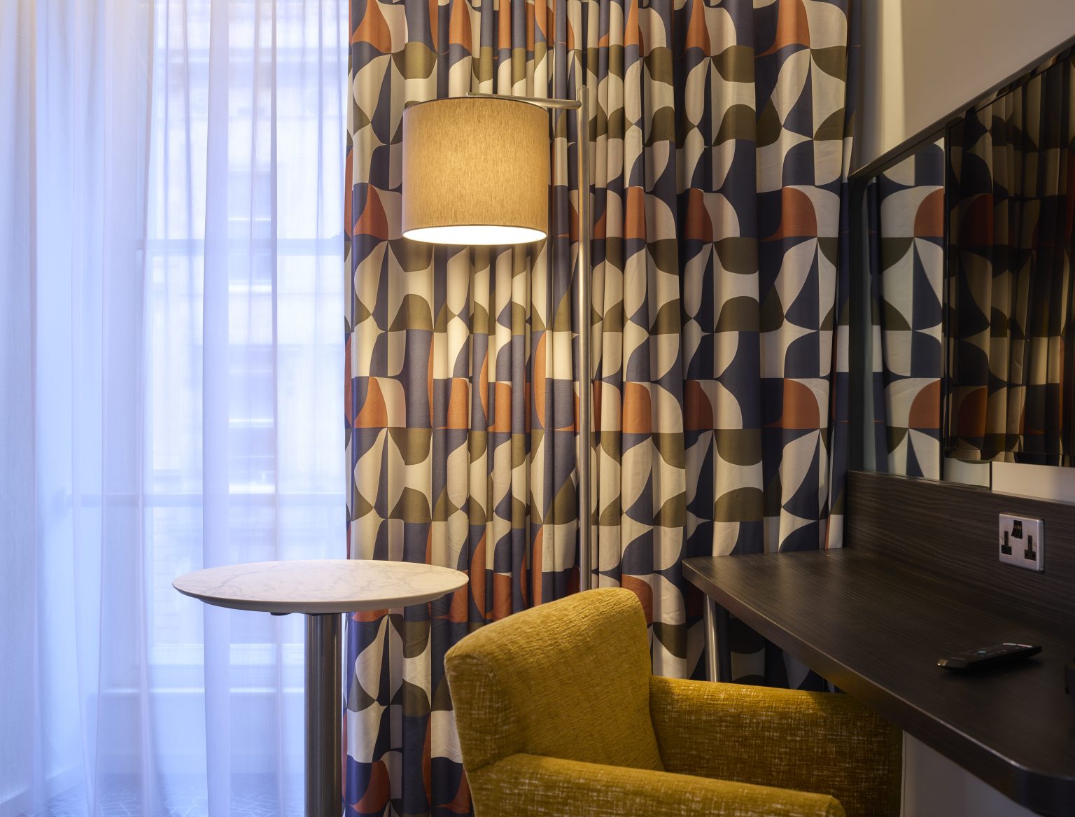 Hotel room with geometric curtains, a soft headboard, and cosy bedding for a stylish and relaxing guest experience.