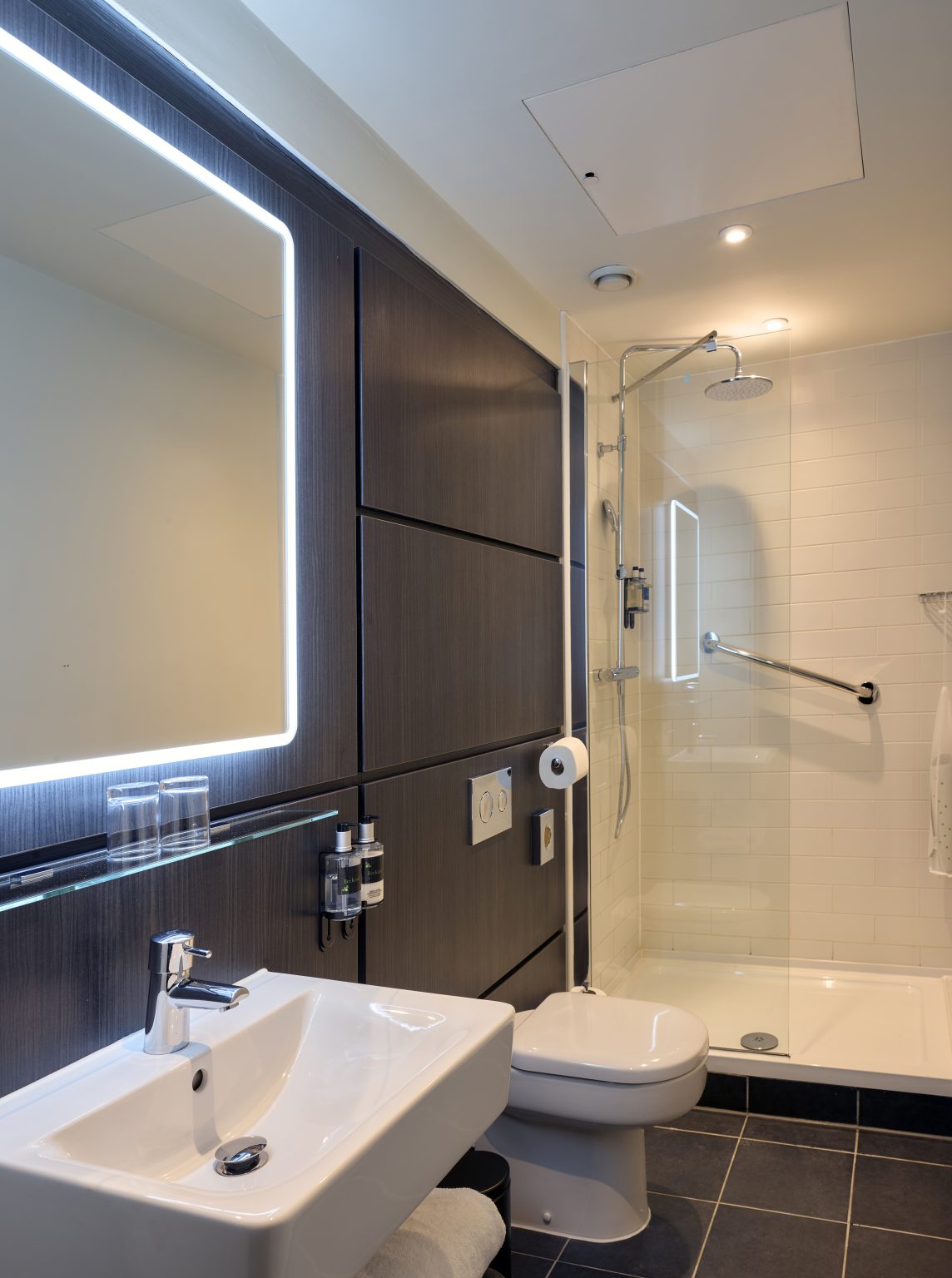 Hotel bathroom featuring brass fixtures, marble tiles, and a walk-in shower for a luxurious and modern fit-out.