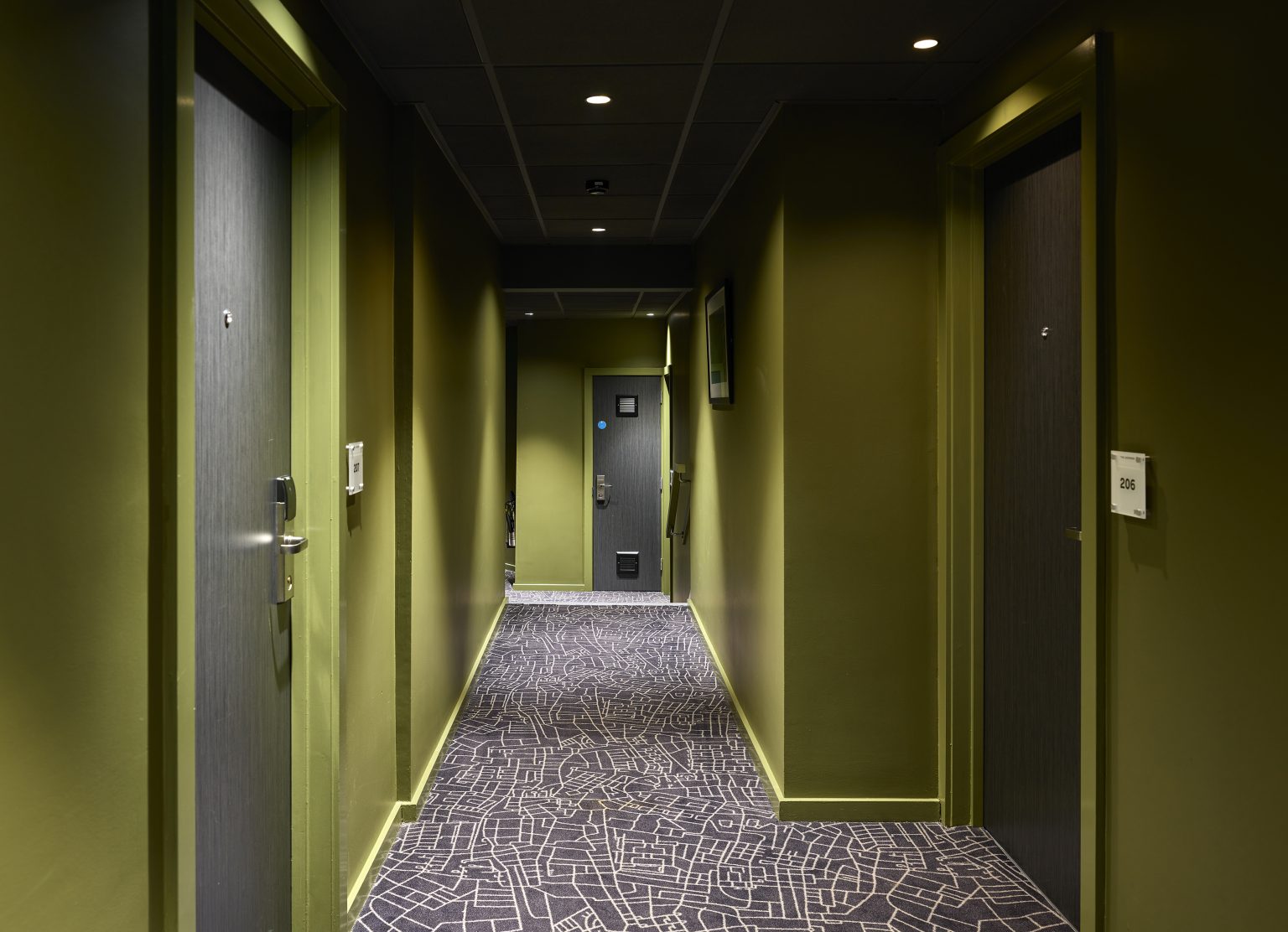 Corridor in a modern hospitality fit-out with bold green walls, patterned carpet, and sleek door finishes for a contemporary guest experience.