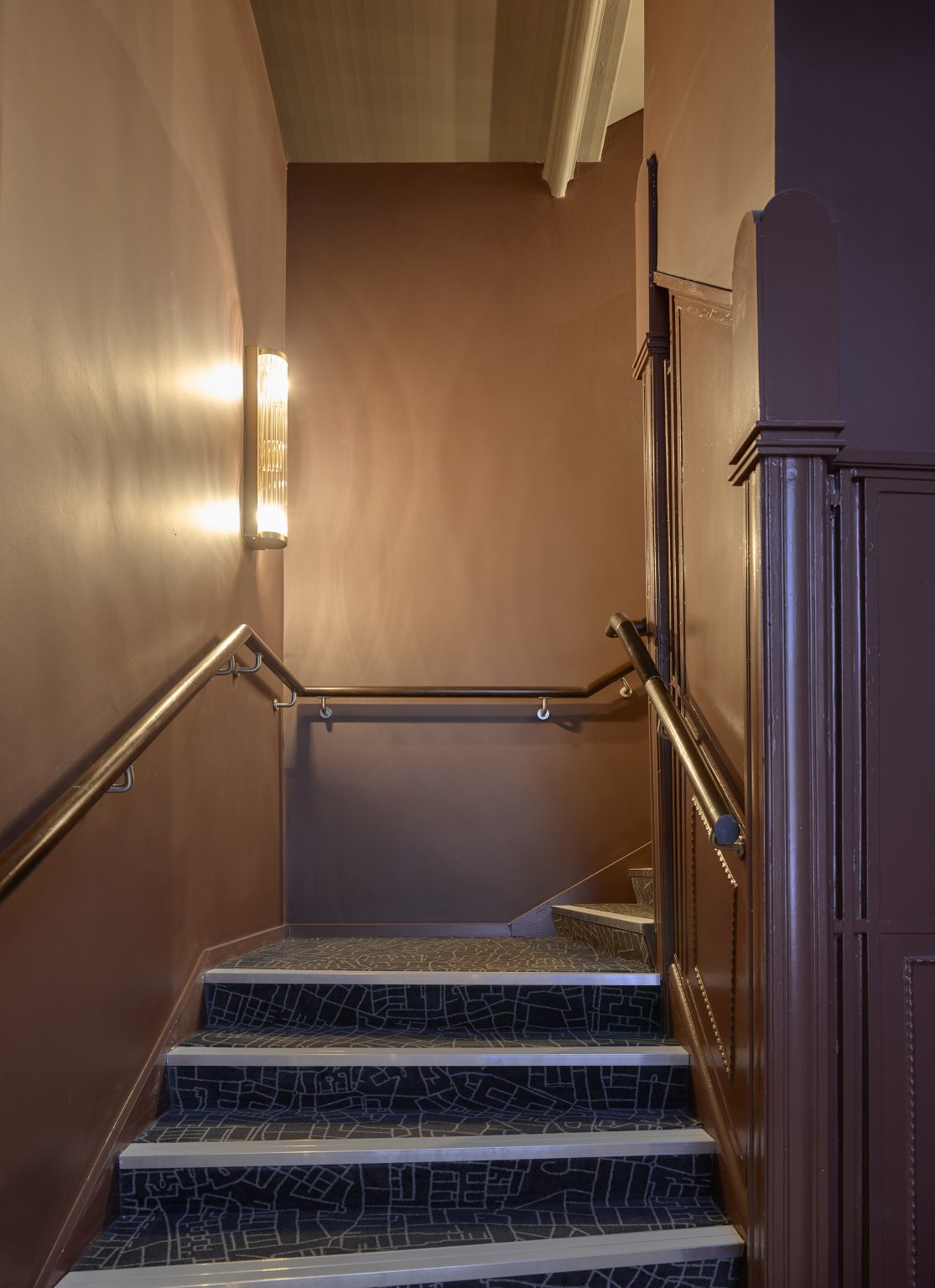 Classic staircase in a hospitality fit-out featuring soft wall lighting, elegant handrails, and patterned carpet for a warm and inviting atmosphere.