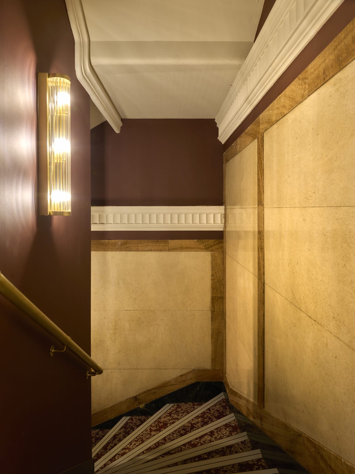 Elegant staircase with classic wall sconces and gold handrails in a luxury hospitality fit-out, featuring intricate architectural details.