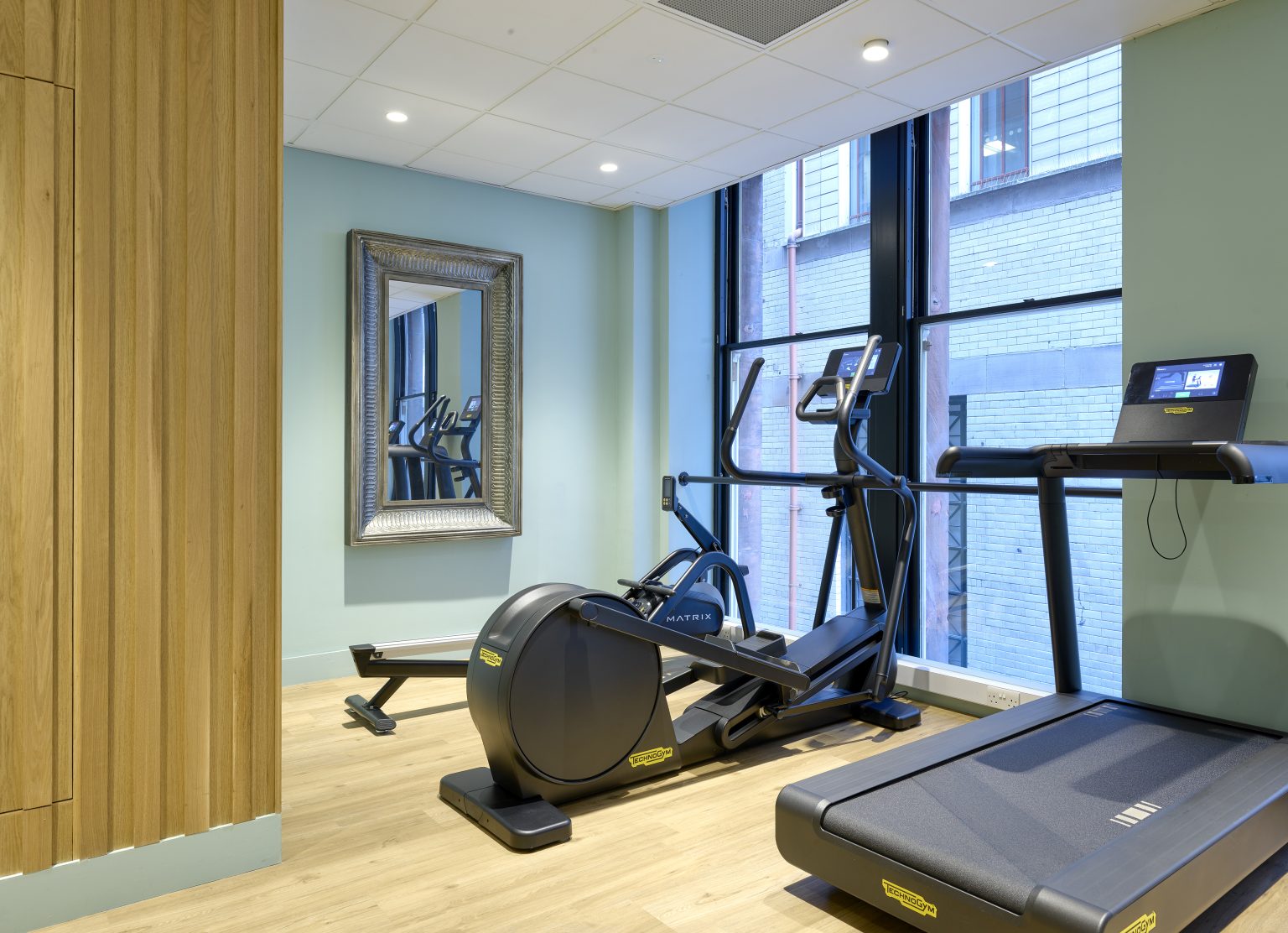 Modern hospitality gym fit-out with high-end fitness equipment, large mirror, and bright natural lighting for a comfortable workout environment.