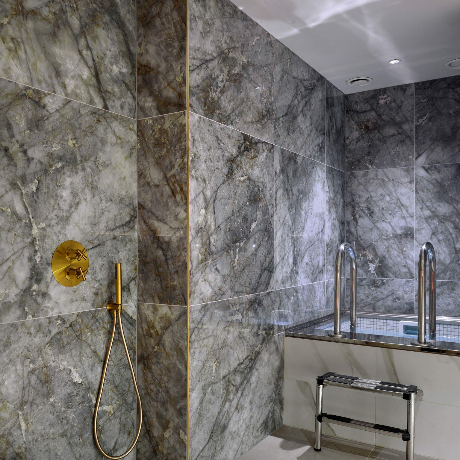 Luxury spa fit-out with marble walls, brass shower fixtures, and a cold plunge pool for a rejuvenating wellness experience.