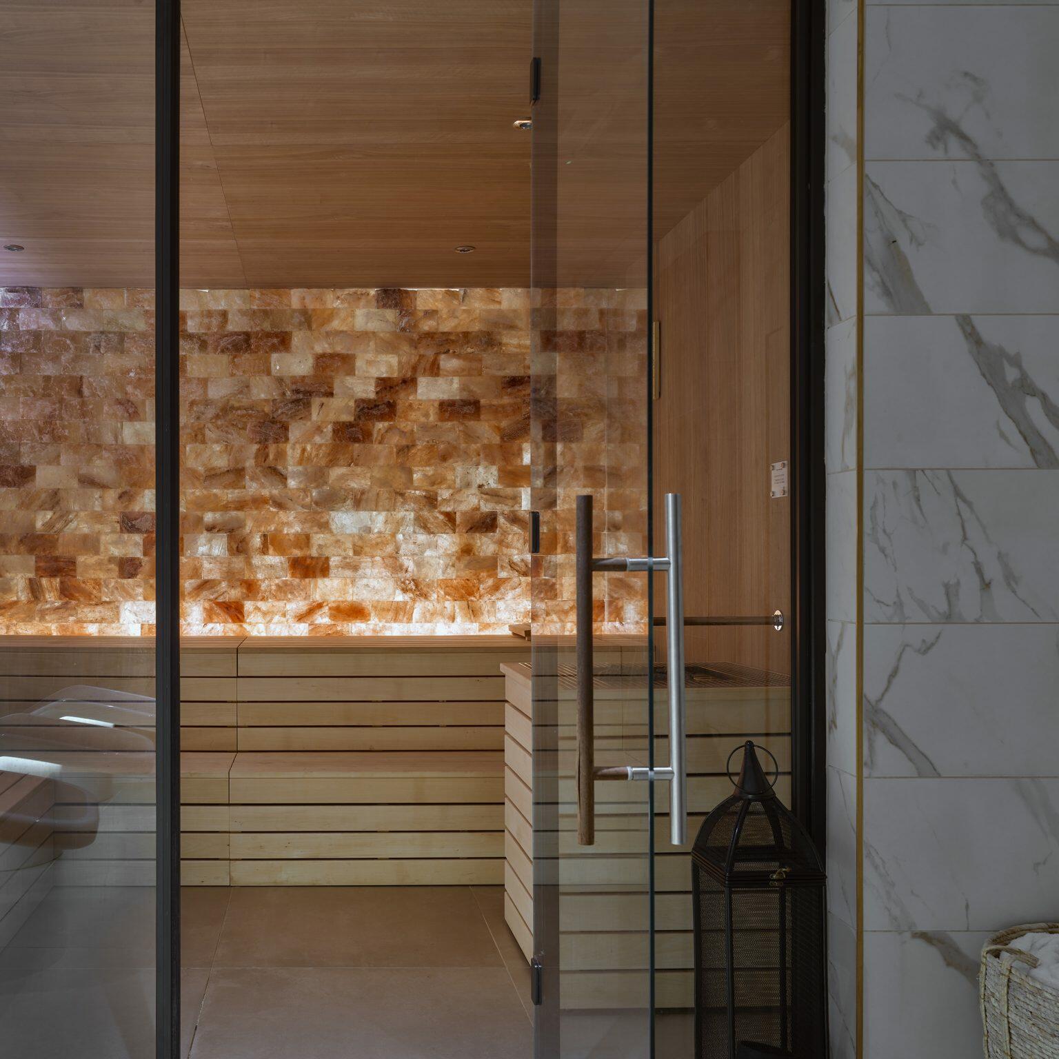 sauna room with warm ambient lighting and glass door, part of a luxury spa fit-out for a relaxing wellness experience.