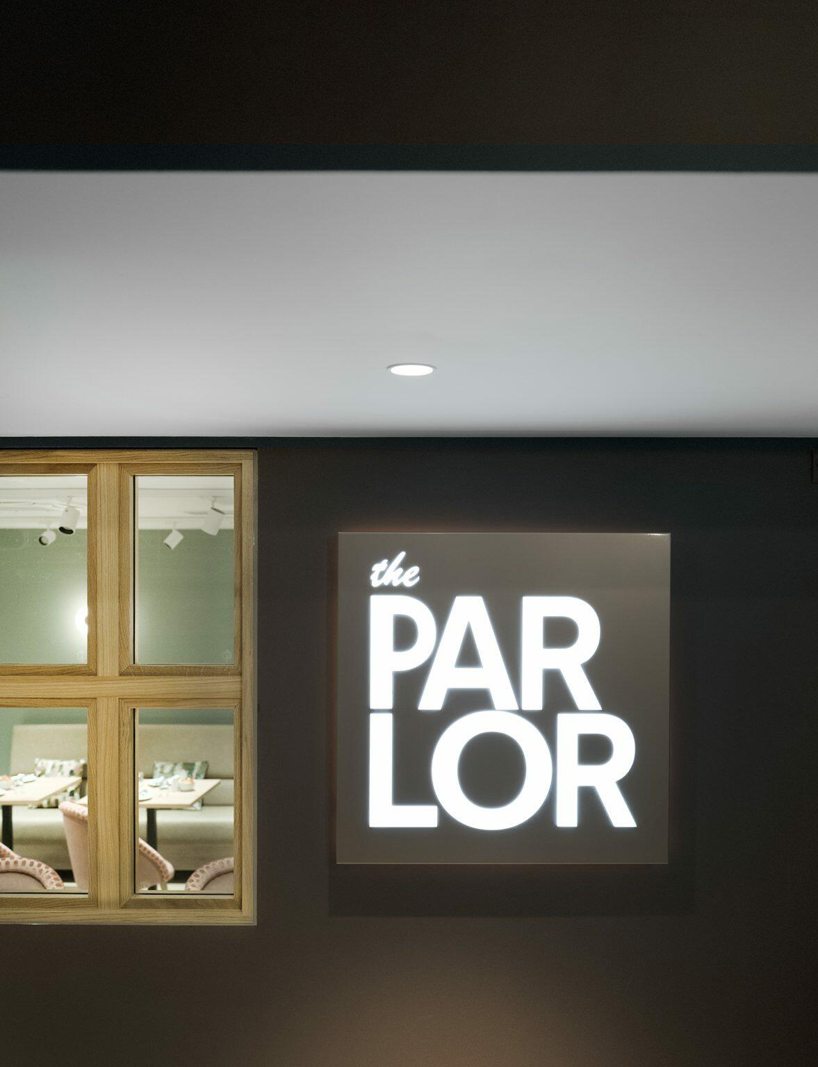 Illuminated sign reading 'The Parlor' at a modern hospitality venue entrance, with a glimpse into the stylish interior dining area.