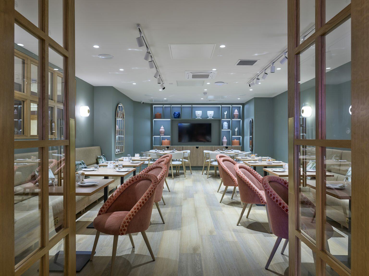 Contemporary hospitality dining area with stylish upholstered chairs, wooden tables, and decorative shelving for a comfortable and modern guest experience.