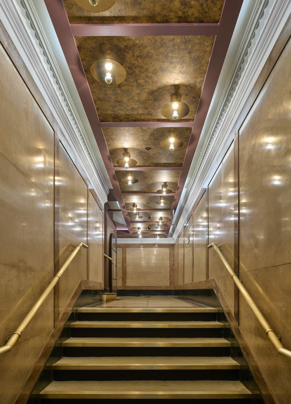 Elegant staircase with gold handrails and artistic ceiling lighting in a luxury hospitality fit-out, creating a sophisticated and welcoming atmosphere.