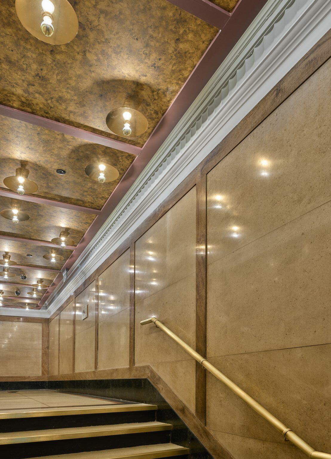 Elegant staircase with gold handrails and artistic ceiling lighting in a luxury hospitality fit-out, creating a sophisticated and welcoming atmosphere.